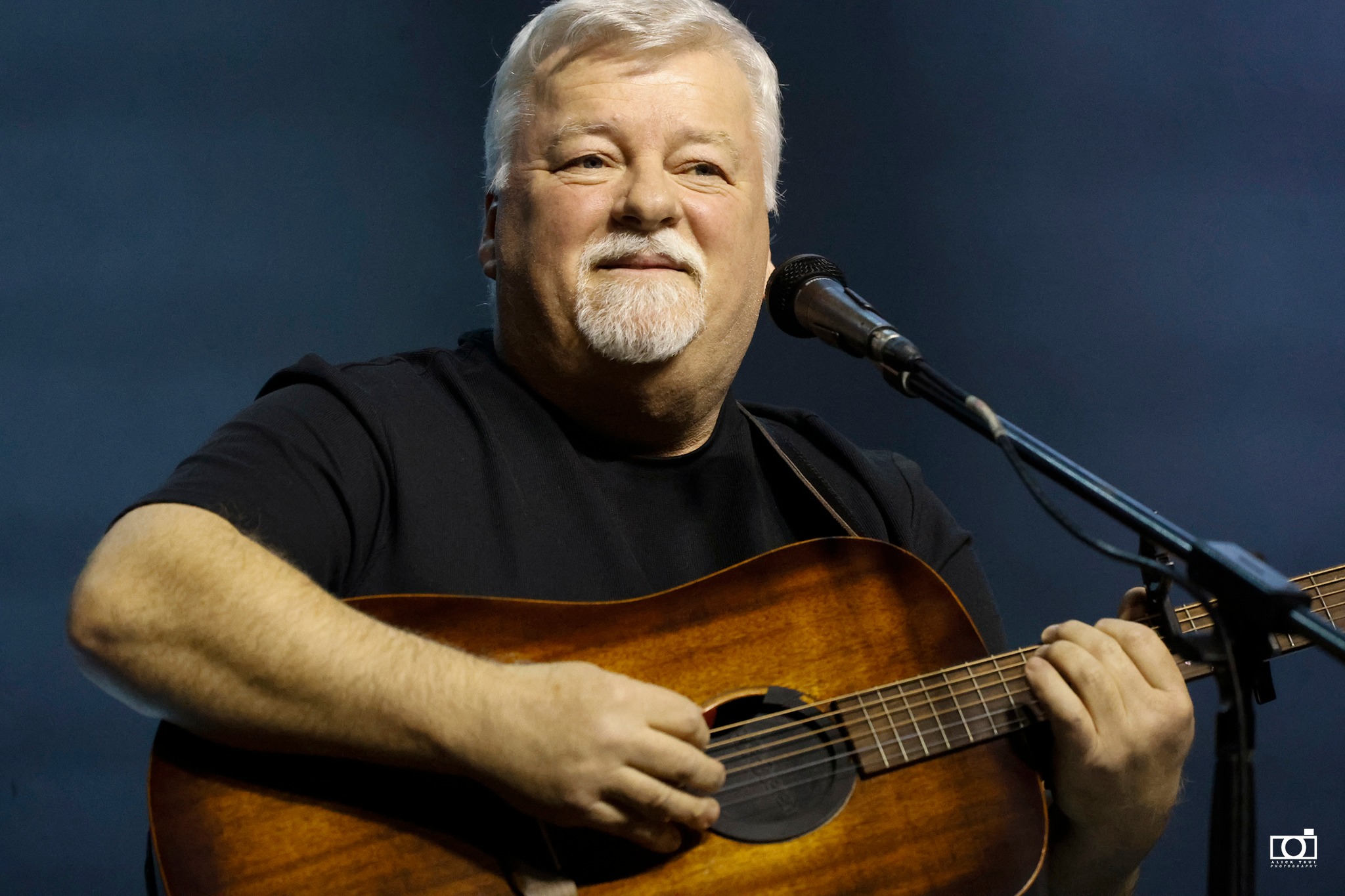 Gordon Cormier smiling onstage with his acoustic guitar